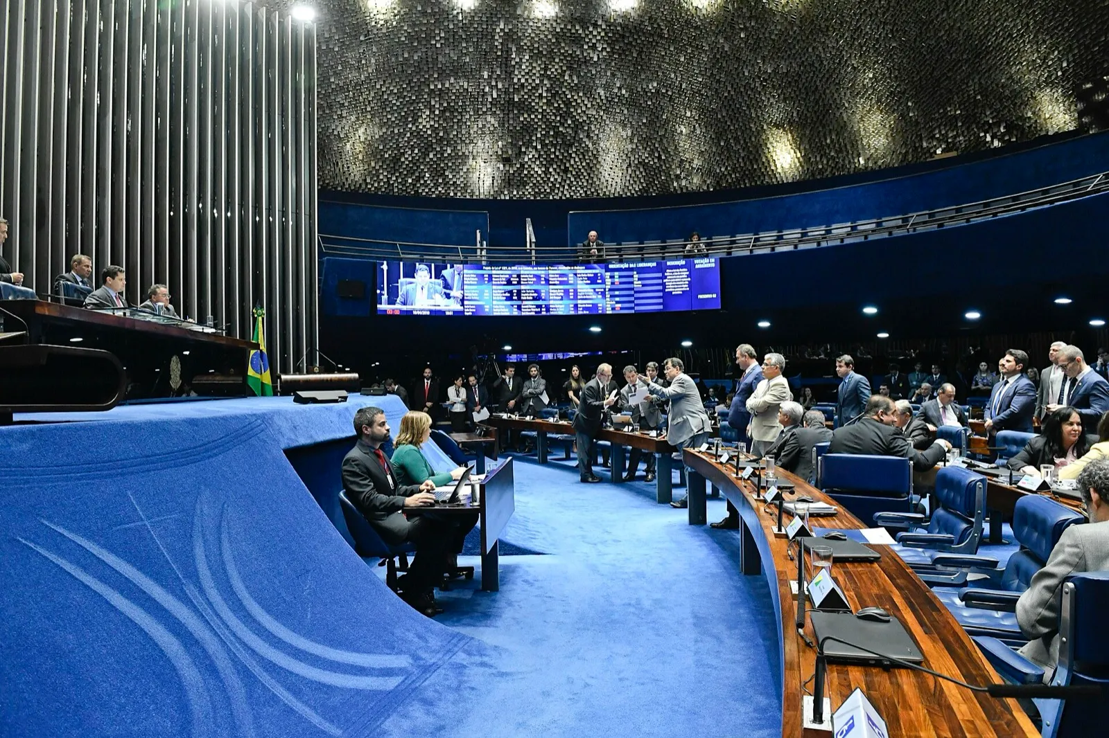 Vista ampla do Plenário do Senado, com a Mesa Diretora à esquerda, senadores nas bancadas azuis e o painel de votação ao fundo.